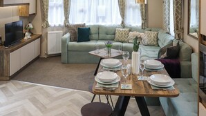 A modern living room with a sofa, dining table set for four, and a television on a stand. - 2 bedroom accommodation in Wisemans Bridge (Wisemans Bridge)