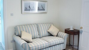 Un sofá a rayas con dos almohadones, un cuadro enmarcado encima y una mesita de madera con un objeto blanco encima.