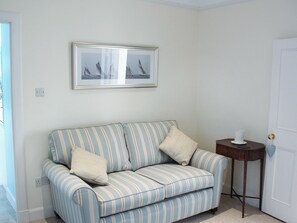 A striped sofa with two pillows, a framed picture above it, and a small wooden side table with a white object on it. - Welcome to Failte, a wonderful four-bedroom house. (Tighnabruaich)
