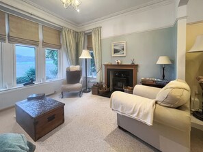 A living room with a fireplace, a sofa, a chair, a wooden chest, and a view of the outdoors. - Welcome to Failte, a wonderful four-bedroom house. (Tighnabruaich)