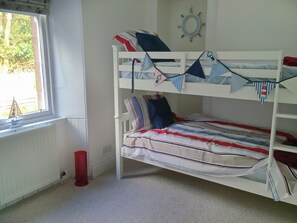 A bunk bed with striped bedding, a ship's wheel decoration, and a window with a view of greenery. - Welcome to Failte, a wonderful four-bedroom house. (Tighnabruaich)