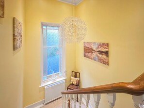 A staircase with a wooden handrail, a white-framed window with a view of greenery, and two wall-mounted artworks. - Welcome to Failte, a wonderful four-bedroom house. (Tighnabruaich)