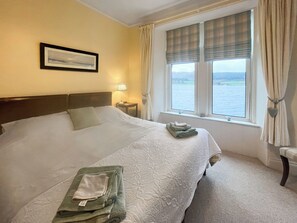 A hotel room with a large bed, a framed picture on the wall, a window with curtains, and a view of the water. - Welcome to Failte, a wonderful four-bedroom house. (Tighnabruaich)