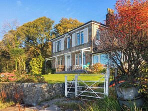 A two-story house with a porch, a stone wall, and a metal gate. - Welcome to Failte, a wonderful four-bedroom house. (Tighnabruaich)