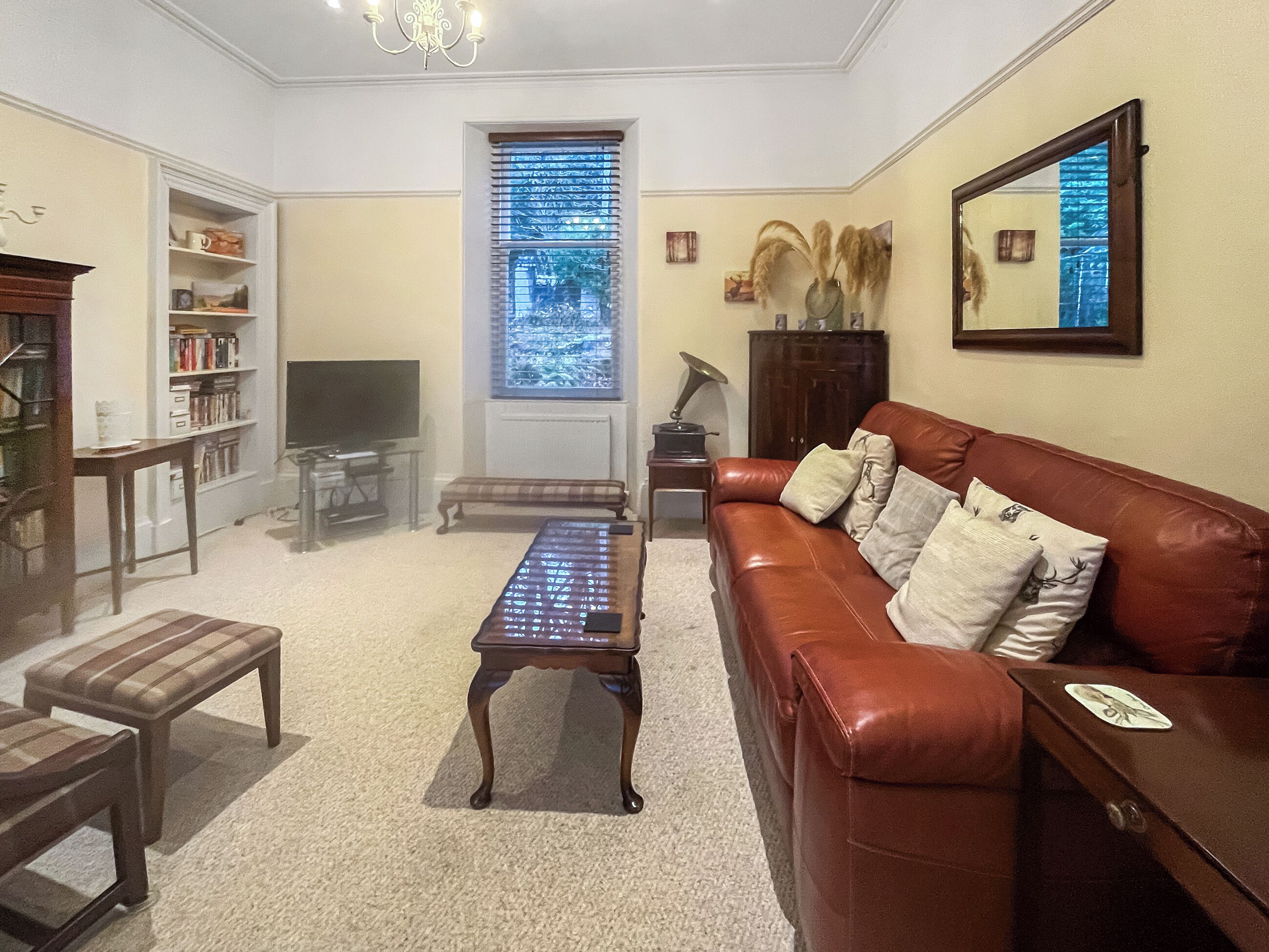 A living room with a brown leather sofa, a coffee table, a bookshelf, a television, and a window with blinds.