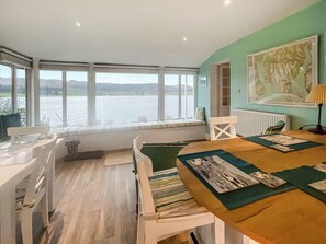 A room with a large window overlooking a body of water, a dining table with placemats, and a radiator. - Welcome to Failte, a wonderful four-bedroom house. (Tighnabruaich)