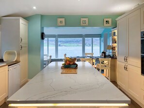 A kitchen with a marble island, white cabinets, and a view of a body of water through large windows. - Welcome to Failte, a wonderful four-bedroom house. (Tighnabruaich)