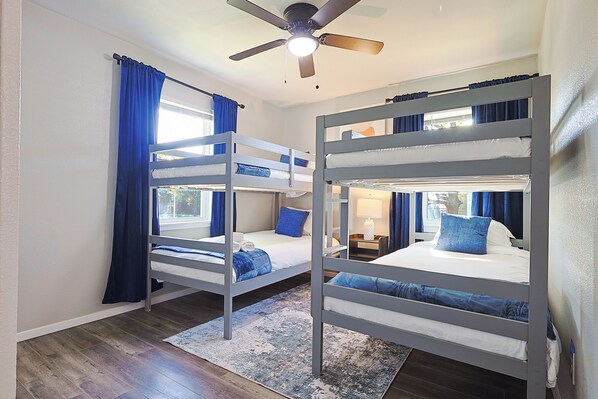 A room with bunk beds, a ceiling fan, and a window with curtains.