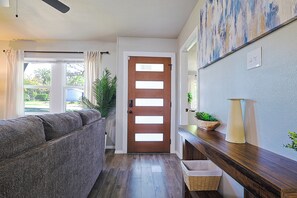 A hallway with a wooden door, a gray sofa, a wooden console table, and a potted plant.