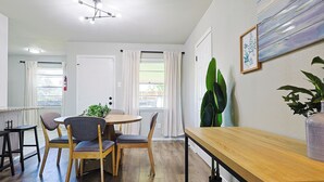 Uma sala de jantar com uma mesa redonda e quatro cadeiras, um banco de madeira e um vaso com planta.