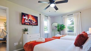 Quarto de hotel com cama, ventilador de teto, televisão exibindo uma chama e janela com cortinas.