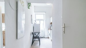 En smal gang med et spisebord og stole, en radiator, et vindue og en vaskemaskine i baggrunden.