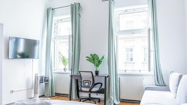 Et moderne hotelværelse med en seng, et skrivebord med stol, en potteplante og et fjernsyn på væggen.