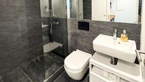 Un baño moderno con ducha de vidrio, inodoro blanco y lavamanos blanco con dispensador de jabón.