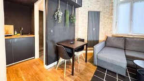 Una cocina moderna con encimera de madera y fregadero, un área de comedor con mesa y sillas, y un sofá gris en una habitación con paredes de ladrillo visto y un ventanal grande.