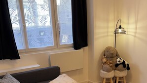 A modern living room with a grey sofa, a small table with stuffed animals, a floor lamp, and a window with decorative curtains. - Comfort in Le Mont-Dore - Pets allowed (Mont-Dore)