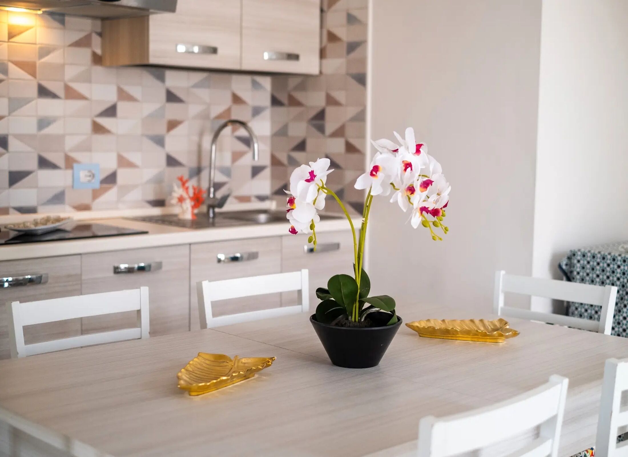 A modern kitchen with a geometric tile backsplash, a sink, and a dining table with chairs.