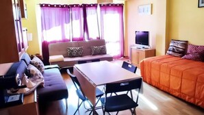 Ein kleines Hotelzimmer mit Sofa, Bett, Esstisch mit Stühlen, Fernseher und einer kleinen Kommode.
