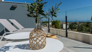 Ein klarer Blick auf einen Balkon mit Tisch, einer gewobenen Vase mit grünen Blättern und einer weit entfernten Skyline.