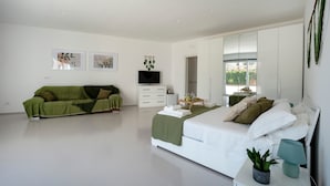 Ein modernes Schlafzimmer mit einem Bett, einem grünen Sofa, einem Fernseher und Kunstwerken an den Wänden.