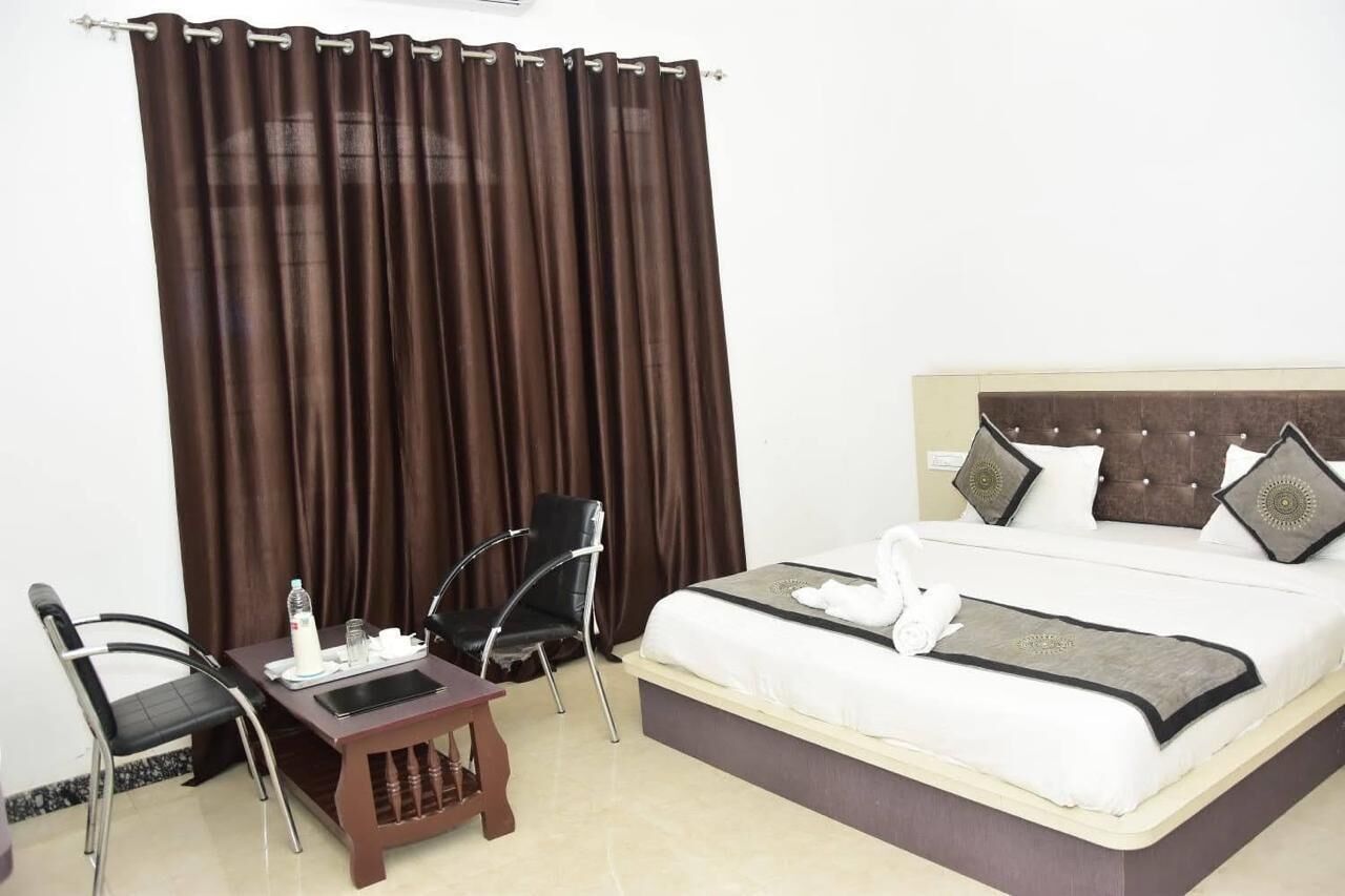 A hotel room with a bed, two chairs, a small table, and a curtain.
