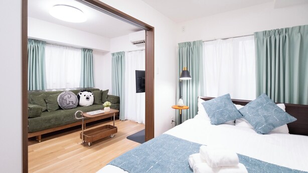Une chambre d’hôtel moderne avec un grand lit, un canapé et une petite table. On y trouve une fenêtre avec des rideaux, un téléviseur fixé au mur et un luminaire au plafond.