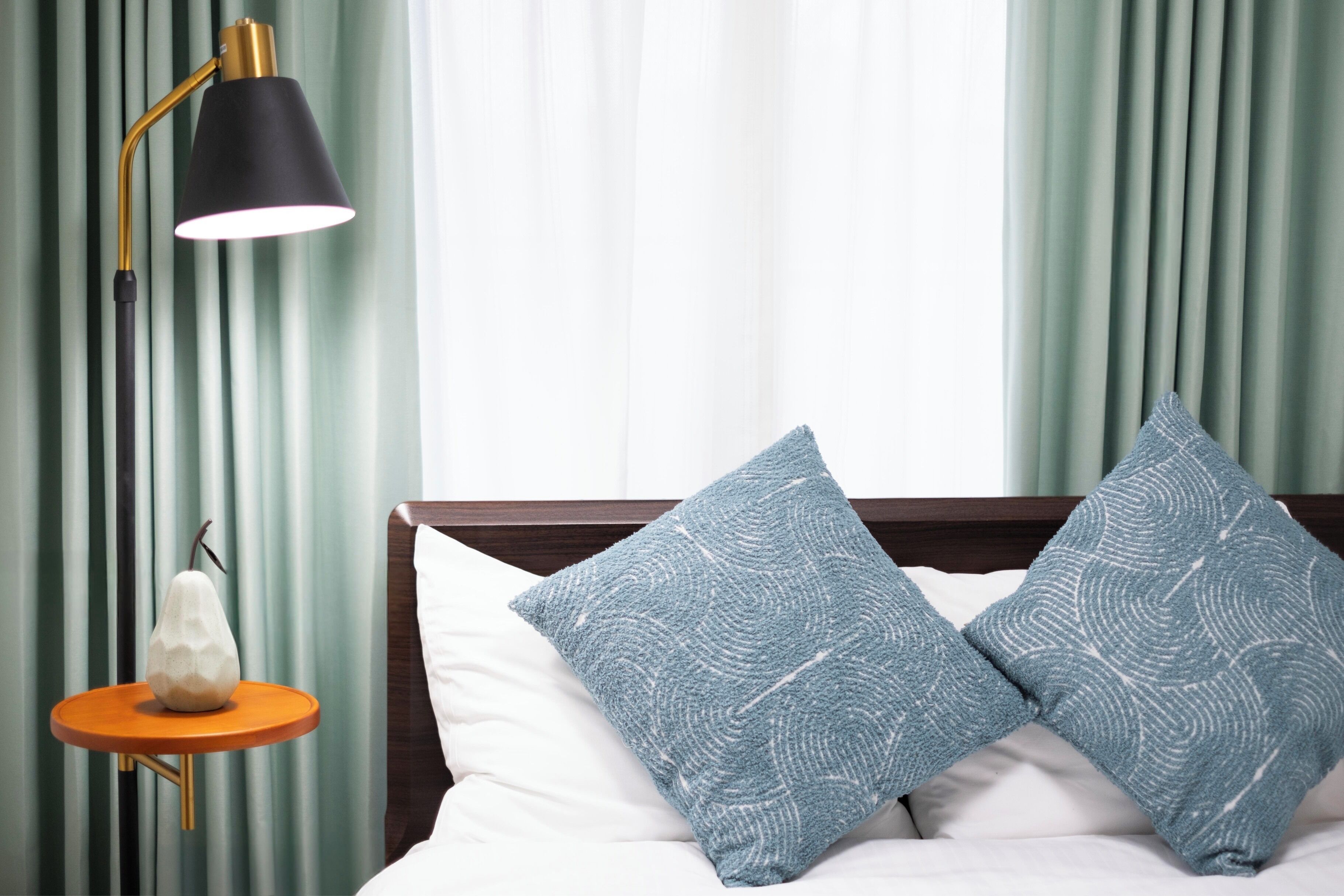 A bed with two patterned pillows, a bedside lamp, and a small table with a pear-shaped object.