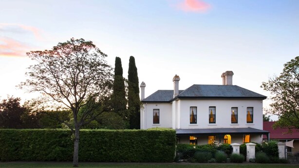 A white two-story house with a dark roof, surrounded by well-maintained hedges and tall trees. - Months & Seasons - Historic 1860s Estate - Daylesford (Daylesford - Hepburn Springs)