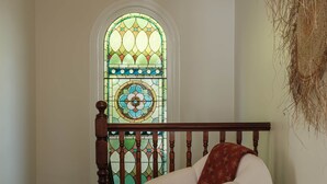 A staircase with a wooden handrail and a white chair with a red throw pillow. A round black table is in front of the chair. A decorative hanging is visible on the wall. - Months & Seasons - Historic 1860s Estate - Daylesford (Daylesford - Hepburn Springs)