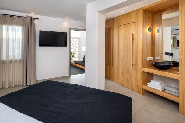 Una habitación de hotel moderna con una cama grande, un armario de madera, un televisor de pantalla plana y un baño con lavamanos y espejo.