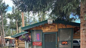 A rustic log cabin with a sign reading "Powderhorn Cabins Office" and an "OPEN" sign on the door.