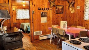 A cabin interior with wooden walls, a dining table with chairs, a stove, and a refrigerator.