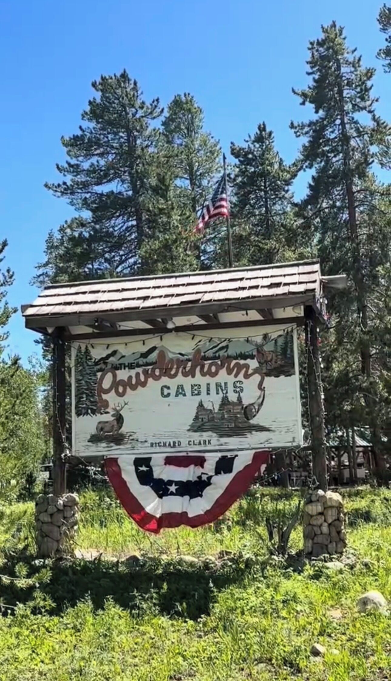 A rustic wooden sign with a painted landscape and the name 'Cowderhorn Cabins' along with 'Richard Clark'.