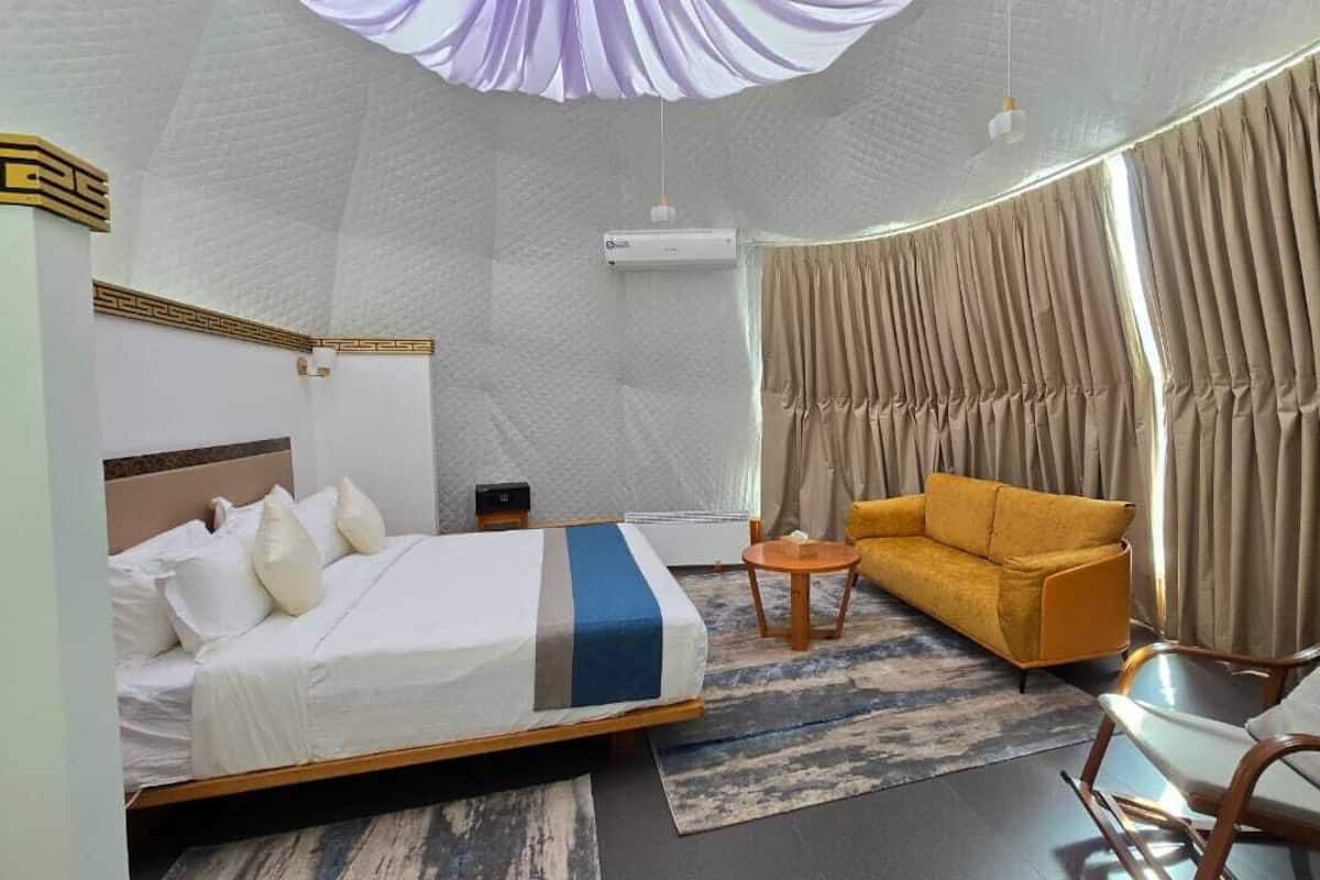 Une chambre d’hôtel moderne, dotée d’un grand lit, d’un canapé, d’un fauteuil, d’une petite table et d’une grande fenêtre avec des rideaux.