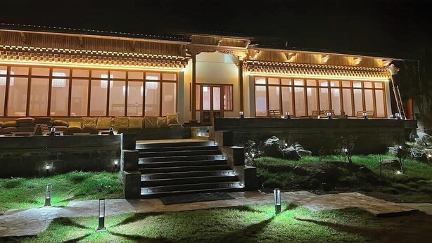 Un edificio tradicional con una entrada bien iluminada, un conjunto de escaleras que conducen a la puerta y un pequeño jardín con césped y rocas.