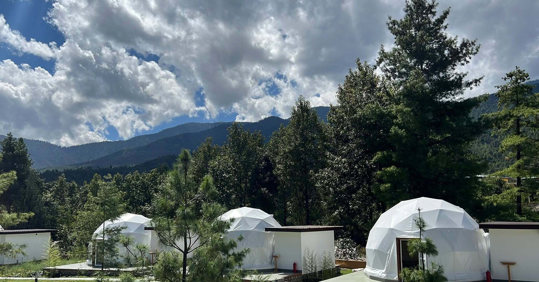 A series of dome-shaped tents in a natural setting with mountains in the background.
