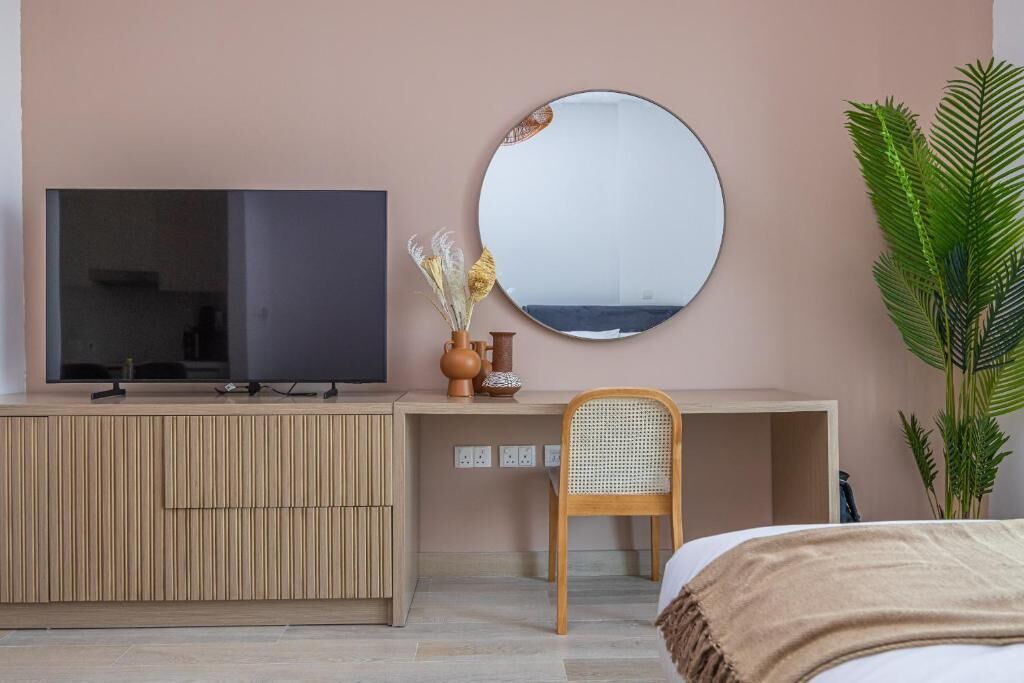 Ein modernes Zimmer mit Fernseher auf einem Holzkasten, einem runden Spiegel, einem Korbstuhl und einer großen Pflanze.
