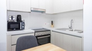Pieni, käytännöllinen keittiö, jossa on valkoiset kaapit, mikroaaltouuni, liesi ja pesuallas.