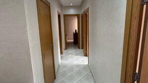 A hallway with white tiled flooring, wooden doors, and a recessed ceiling light. - Charming 3-Bedroom Apartment Near Menara Garden (Marrakesh)