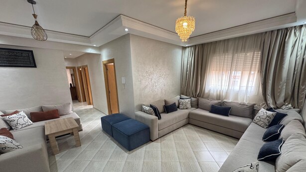 A modern living room with a sectional sofa, a small table, and a blue ottoman. - Charming 3-Bedroom Apartment Near Menara Garden (Marrakesh)
