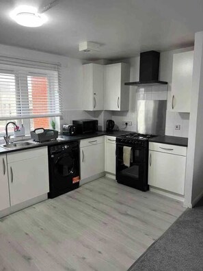 A compact kitchen with white cabinets, a black stove, a microwave, and a washing machine. - Charming 1-Bedroom Apartment in Central London (London)