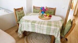 A dining area with a table set for two, featuring a checkered tablecloth, a woven basket with fruits and flowers, and wooden chairs with cushions. - Bright&Spacious Apartment in Sleeps 8 Family& (Lisboa)