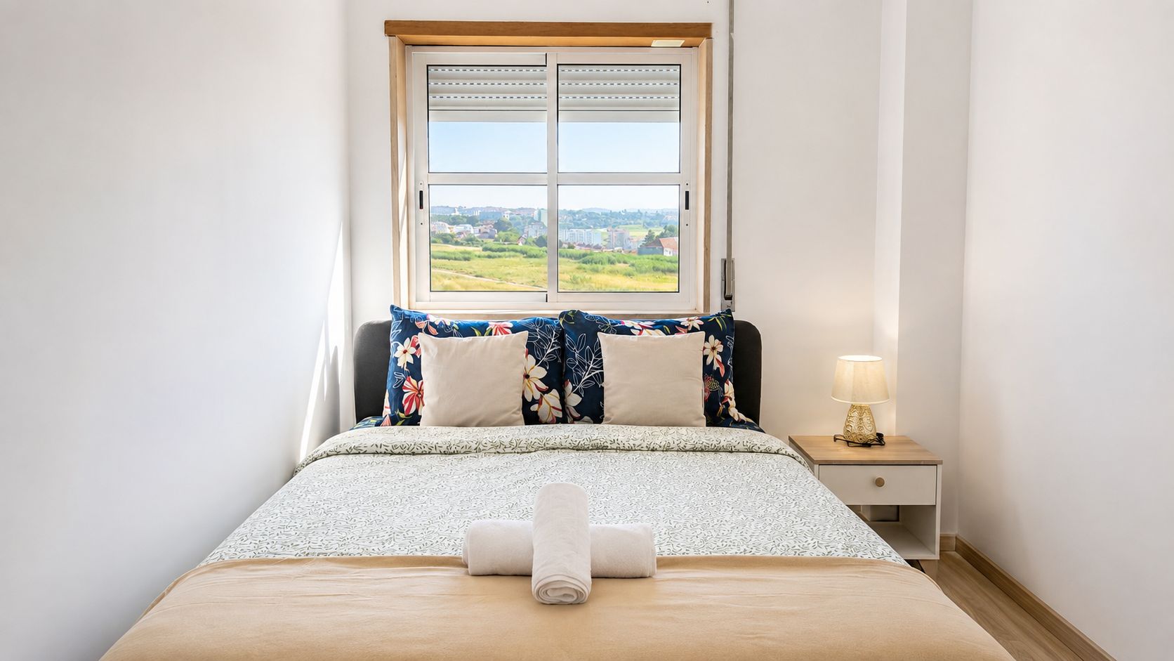 Ein Schlafzimmer mit einem Bett, einem Nachttisch, einer Lampe und einem Fenster mit Landschaftsblick.