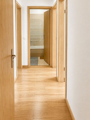 Ein Flur mit Holzdielen und Türen zu einem Zimmer mit Fenster und Jalousien.