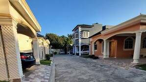 A residential street with houses on both sides, a paved driveway, and parked cars. - TORRE ALTA 1 Bedroom Apt 5B (Puerto Plata)