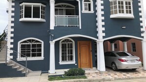 A two-story house with a balcony, a staircase, and a car parked in front. - TORRE ALTA 1 Bedroom Apt 5B (Puerto Plata)