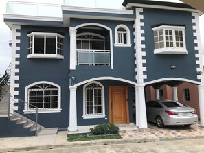 A two-story house with a balcony, a staircase, and a car parked in front. - TORRE ALTA 1 Bedroom Apt 5B (Puerto Plata)