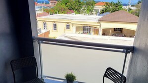 A balcony with two chairs and a small table, a potted plant, and a view of buildings and a clear sky. - TORRE ALTA 1 Bedroom Apt 5B (Puerto Plata)
