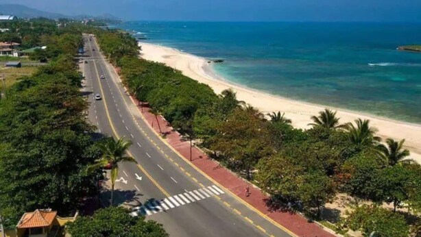 A coastal road with a beach on one side and a road lined with trees and a sidewalk. - TORRE ALTA 1 Bedroom Apt 5B (Puerto Plata)