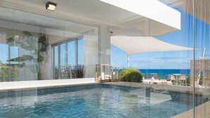 A modern infinity pool with clear blue water, large windows, and a view of the ocean. - Crown Penthouse - Luxury & Views   All inclusive (Puerto Plata)
